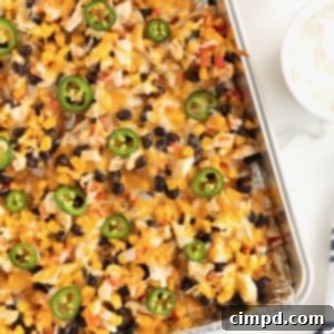 Loaded One Pan Chicken Black Bean Nachos 10 An aluminum sheet pan brimming with golden-brown nachos, beautifully topped with melted cheese, hearty black beans, and perfectly arranged jalapeño slices.