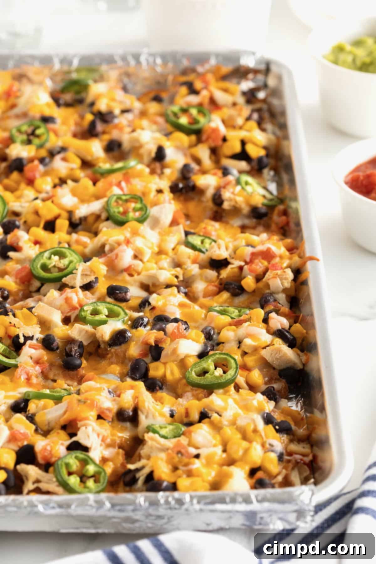 Loaded One Pan Chicken Black Bean Nachos 4 An aluminum sheet pan overflowing with colorful nachos, beautifully topped with golden-brown cheese, shredded chicken, hearty black beans, sweet corn, and vibrant jalapeño slices.