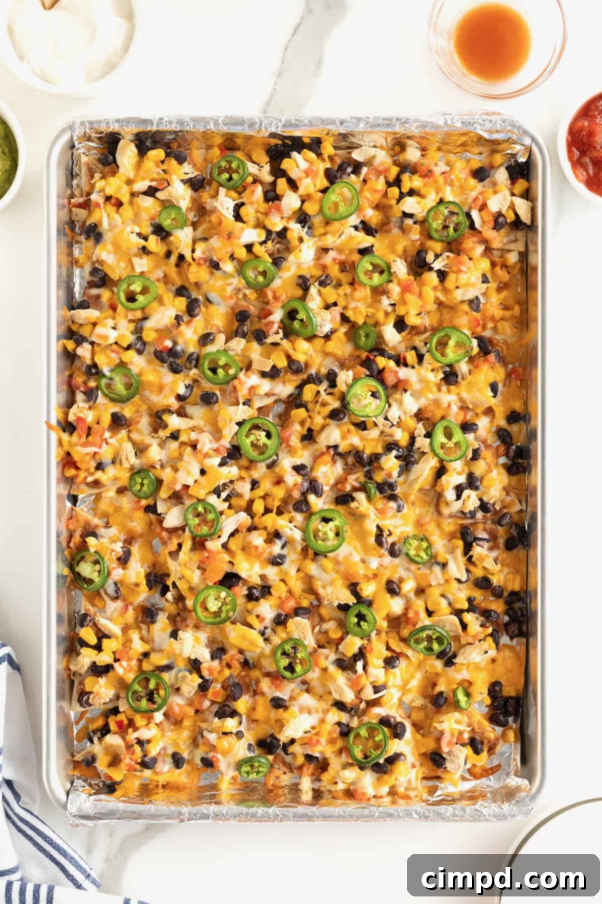 Loaded One Pan Chicken Black Bean Nachos 7 A vibrant aluminum sheet pan brimming with golden-brown nachos, beautifully topped with melted cheese, hearty black beans, and perfectly arranged jalapeño slices.
