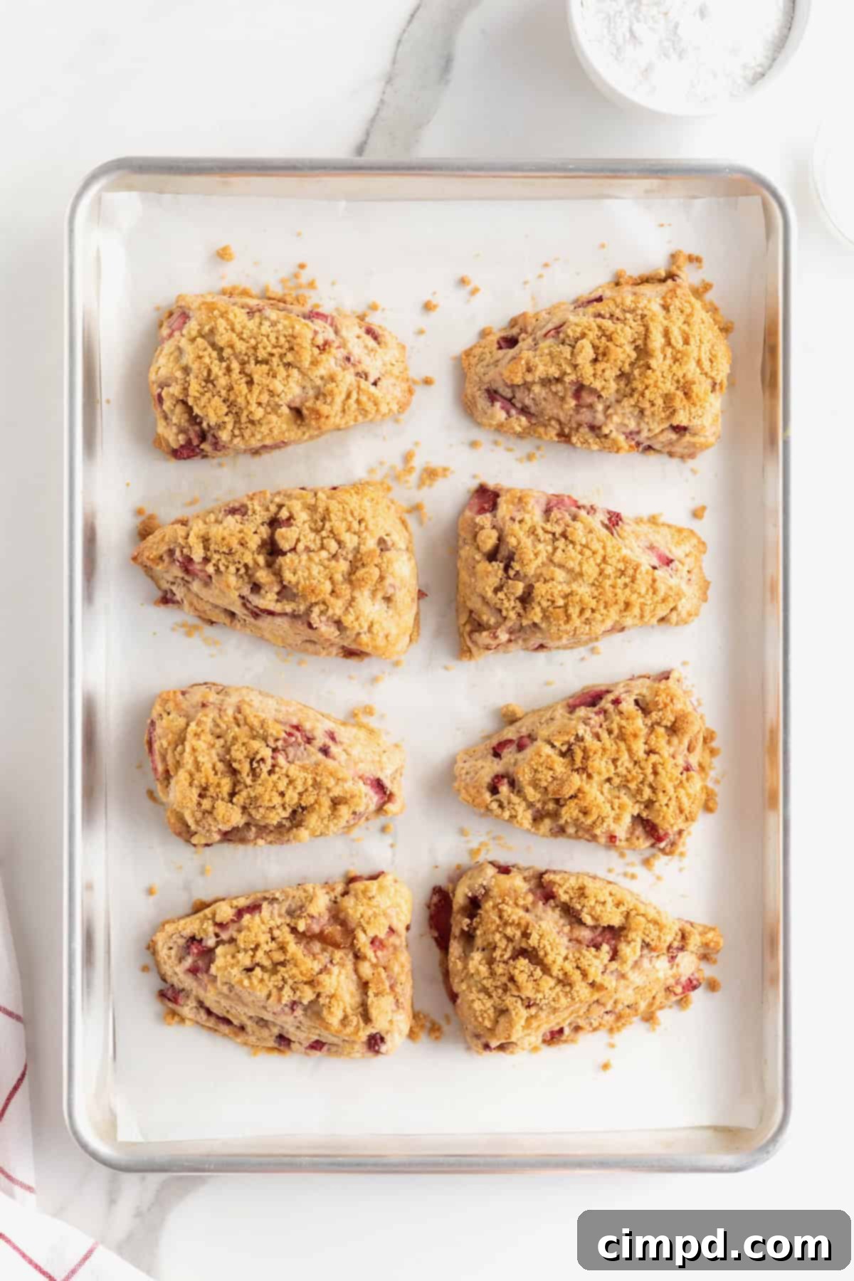 Eight perfectly baked strawberry streusel scones on a parchment-lined aluminum baking sheet, just out of the oven.