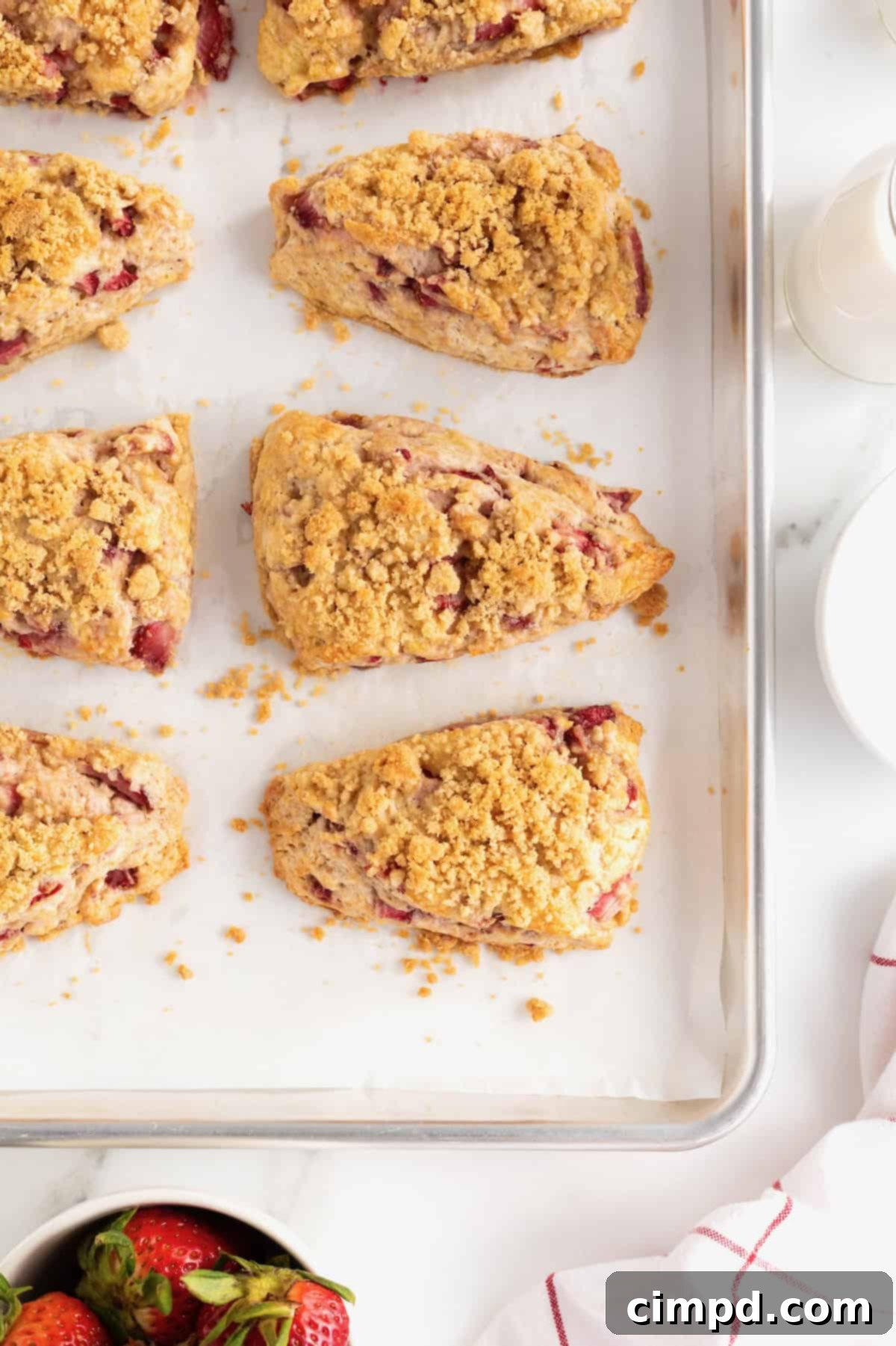 Seven delicious strawberry streusel scones resting on a parchment-lined aluminum baking sheet, highlighting their golden-brown topping.