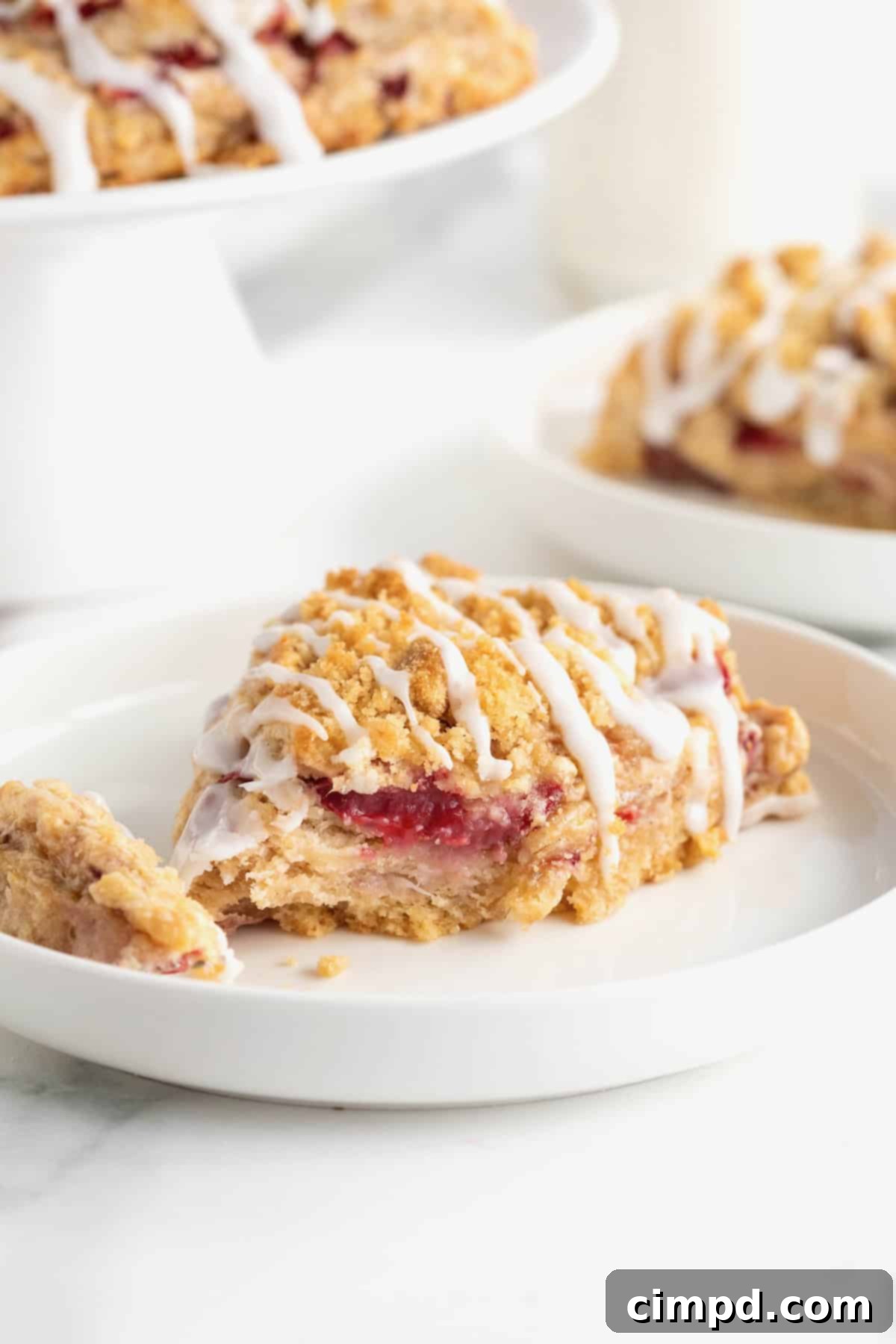 A single strawberry scone, beautifully drizzled with white icing, resting on a pristine white plate with a bite taken out.