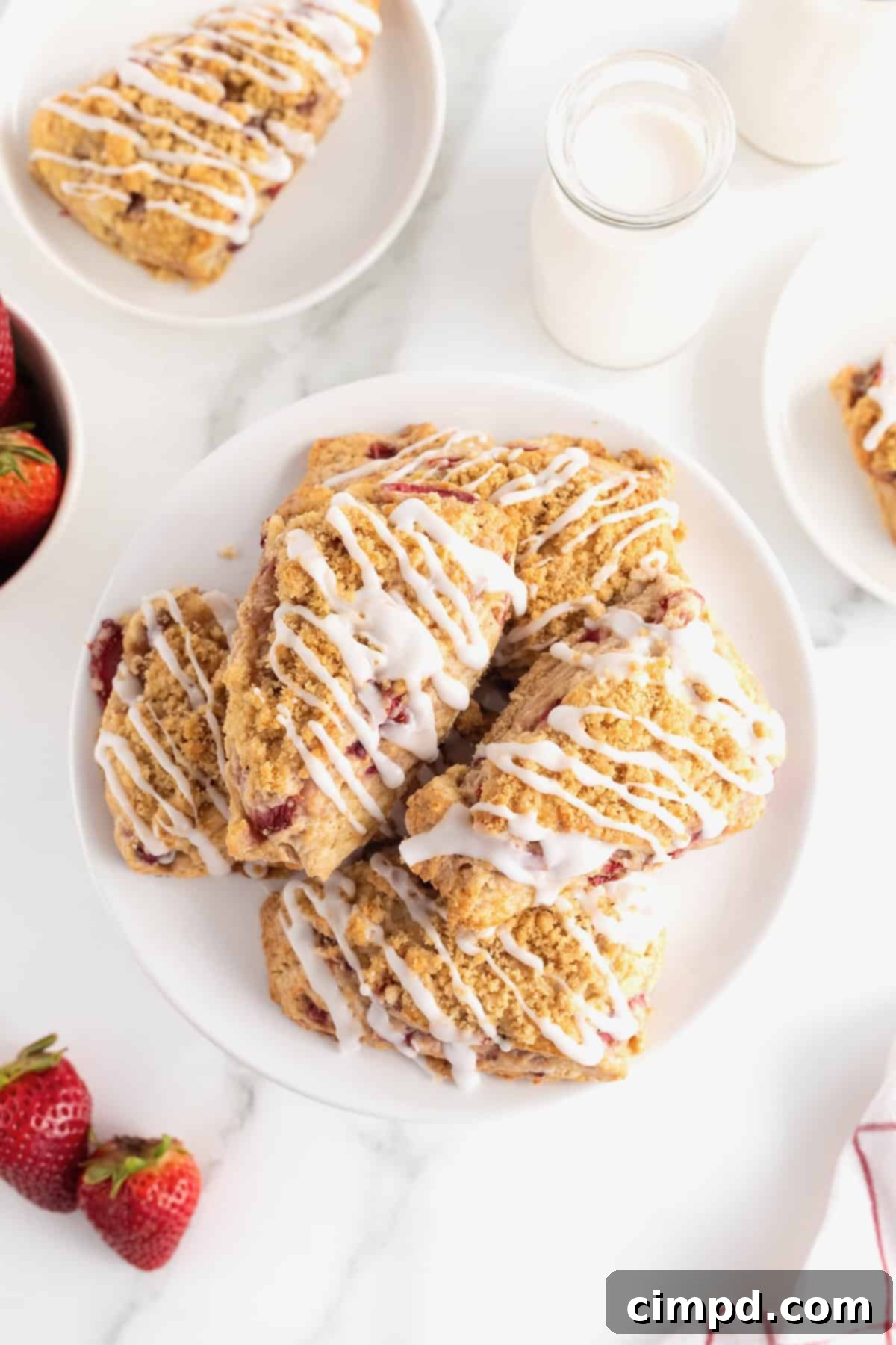 Five strawberry streusel scones, artfully drizzled with white icing, arranged on a white serving platter.