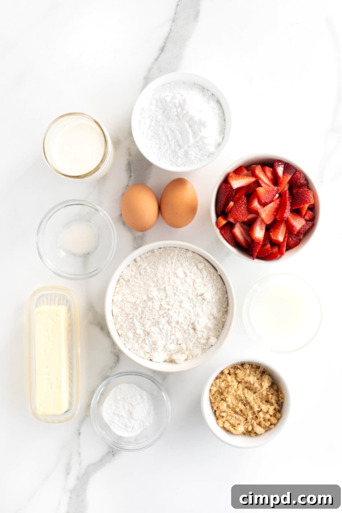 Assorted ingredients for strawberry scones, including flour, sugar, butter, and fresh strawberries, laid out in small white dishes on a white marble surface.