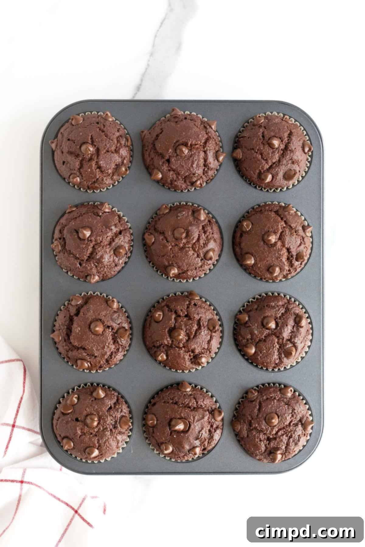A dark aluminum muffin tin filled with freshly baked and perfectly risen double chocolate muffins.