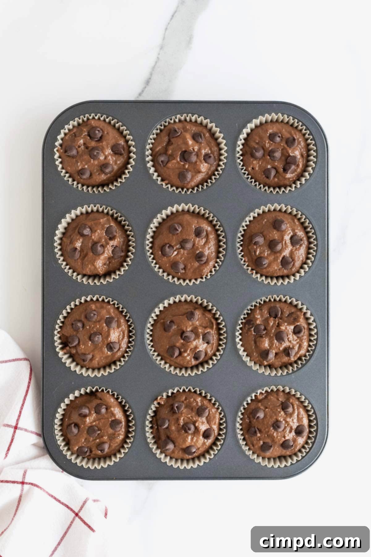 A dark aluminum muffin tin filled with perfectly portioned double chocolate muffin batter, ready for baking.