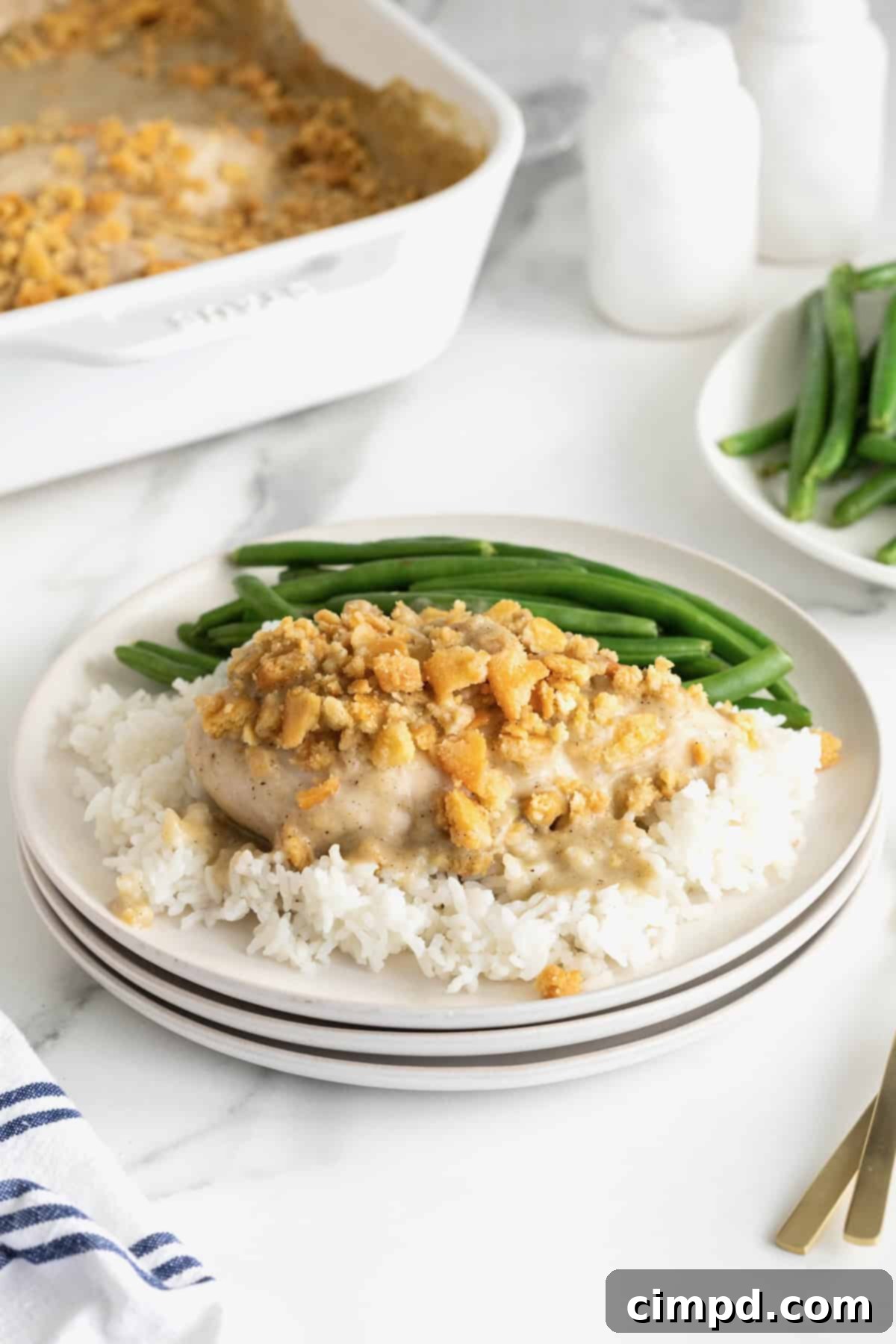 A white dinner plate with a generous serving of creamy chicken bake, perfectly golden and bubbly, resting on a bed of fluffy white rice.