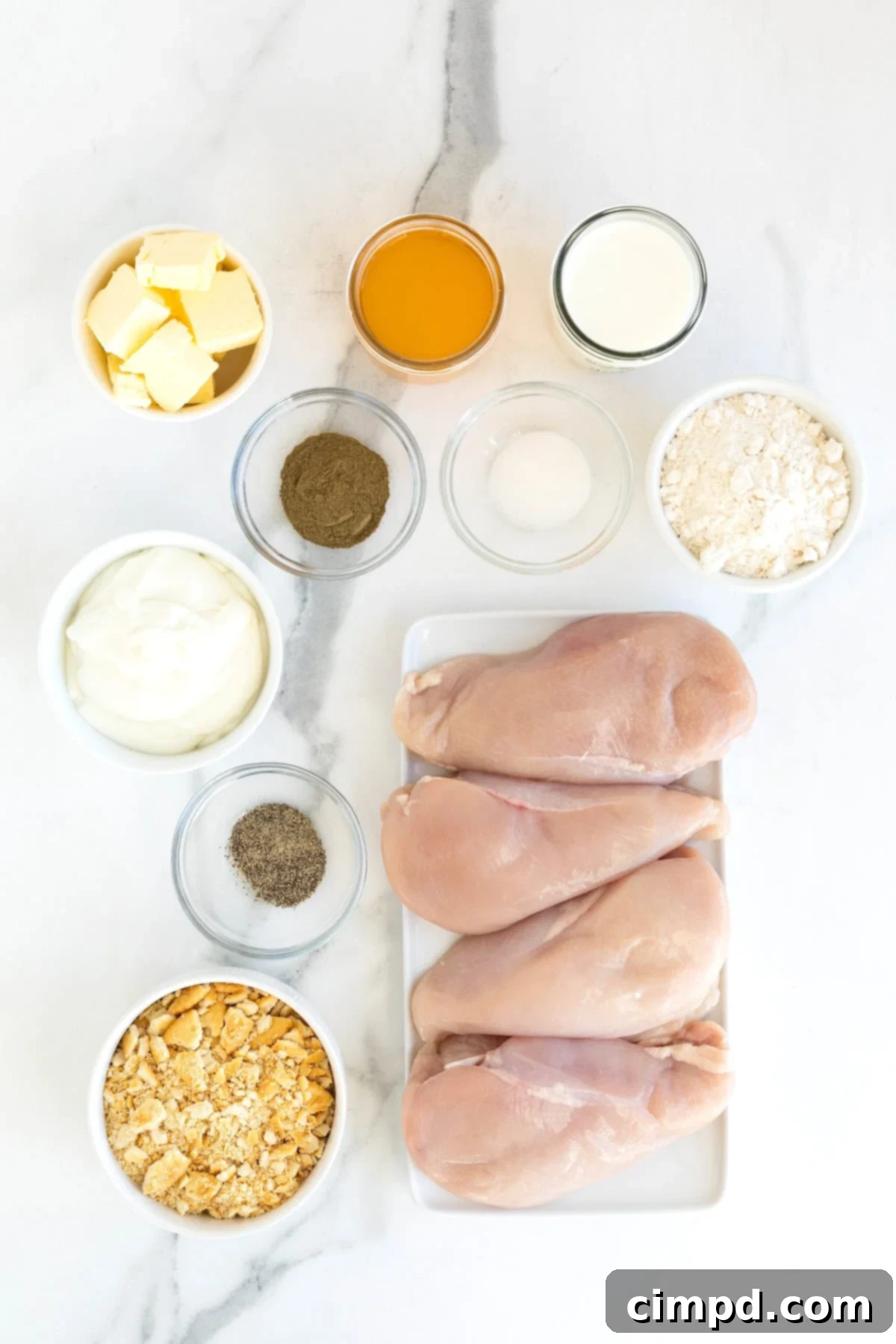 A beautiful flat lay of all the fresh ingredients needed for Creamy Chicken Bake, neatly arranged in small glass dishes on a white marble counter, ready for preparation.