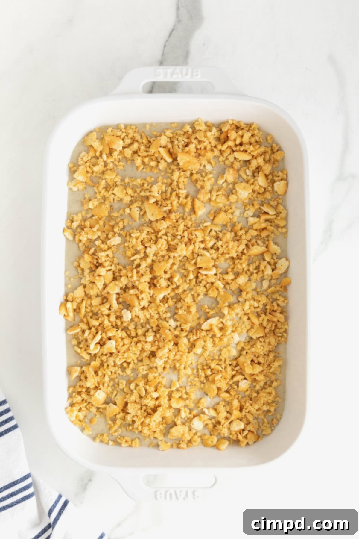 An unbaked creamy chicken casserole in a white ceramic dish, generously topped with a layer of buttery Ritz cracker crumbs, ready for the oven.