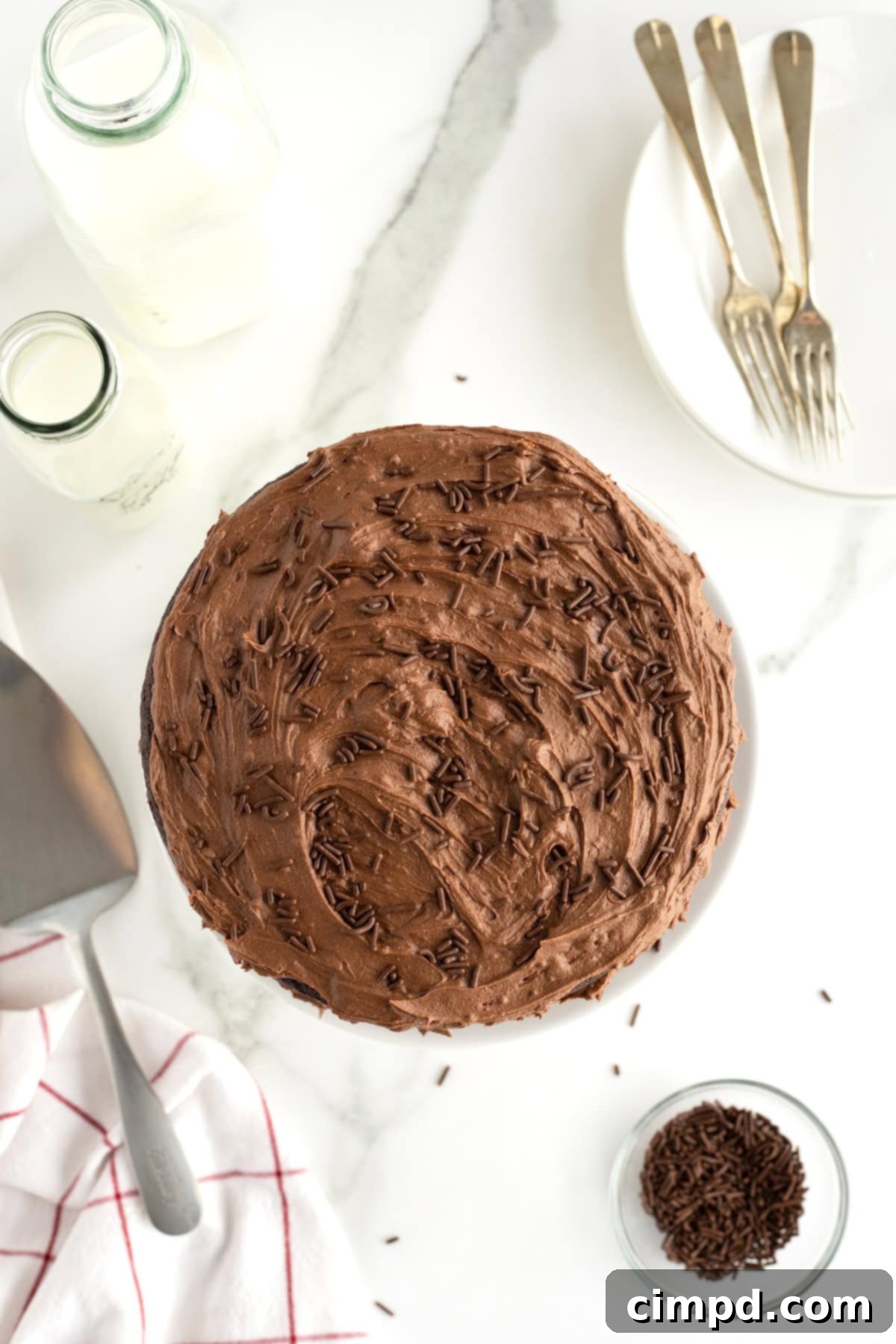 View of the a chocolate cake with chocolate icing and chocolate sprinkles from the top on a white marble counter.