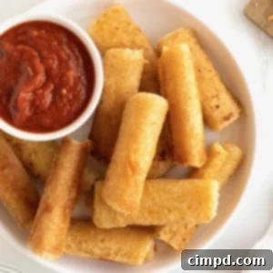 A large white serving plate with a pile of golden-brown grilled cheese roll ups and a small dish of vibrant marinara sauce, perfect for dipping.