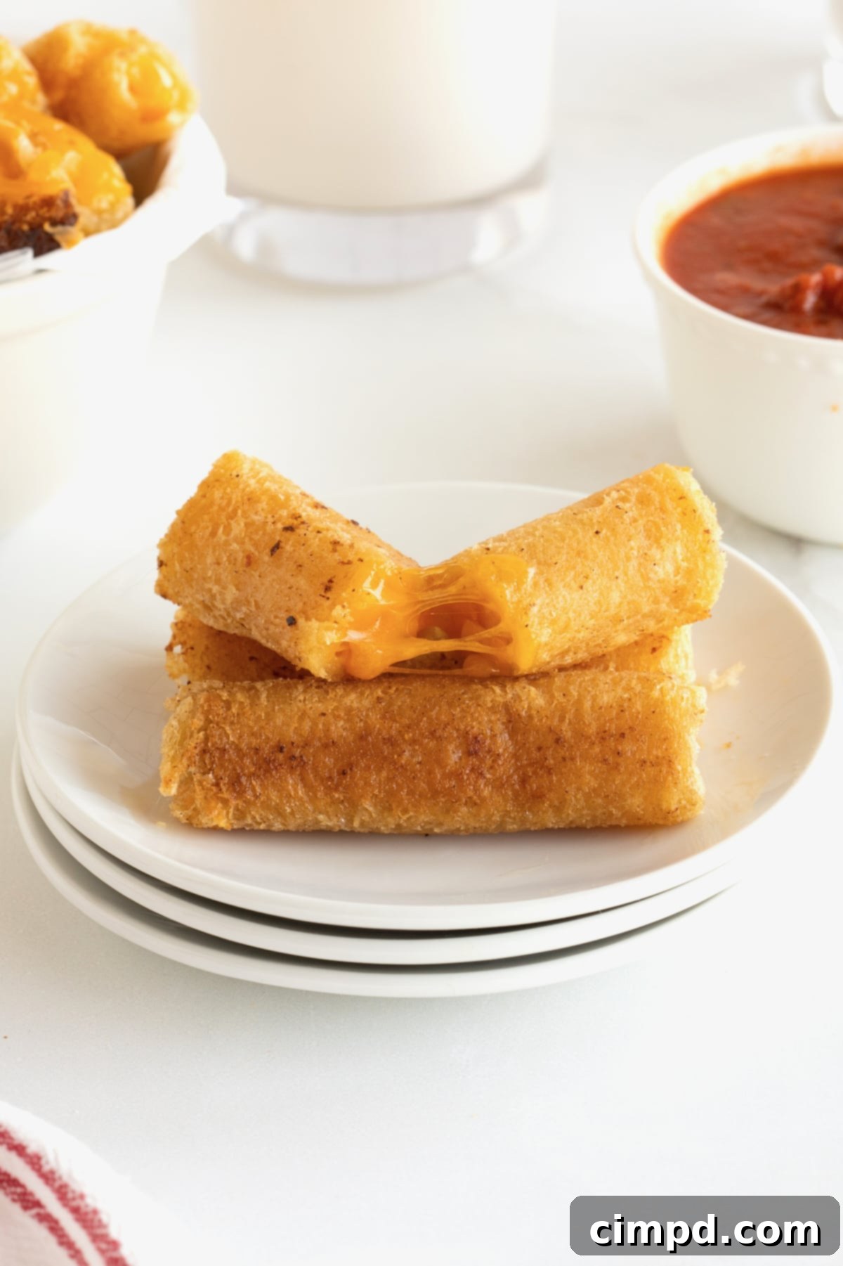 Three perfectly golden-brown grilled cheese roll ups arranged neatly on a pristine white plate. One roll up is thoughtfully cut in half, revealing the warm, melted cheese within, ready to be enjoyed.