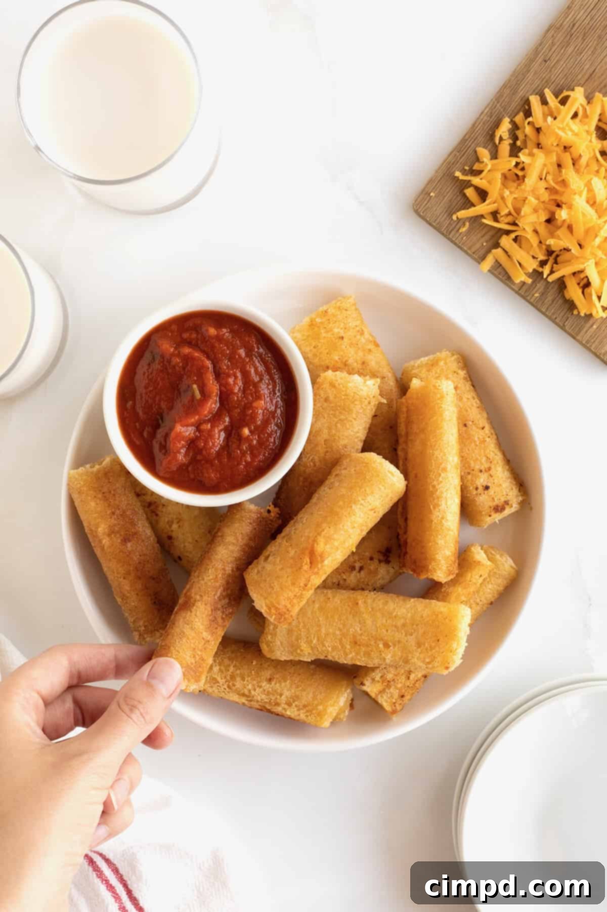 A pristine white serving plate generously filled with golden-brown grilled cheese roll ups, presented alongside a small, inviting dish of vibrant marinara sauce, perfect for dipping.