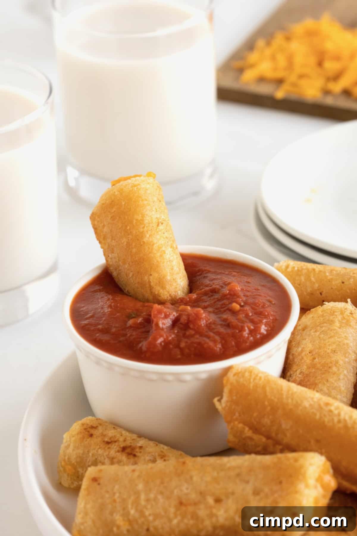 A delectable grilled cheese roll up being dunked into a small, elegant white dish filled with rich marinara sauce, highlighting its crispy exterior and readiness for a flavorful bite.