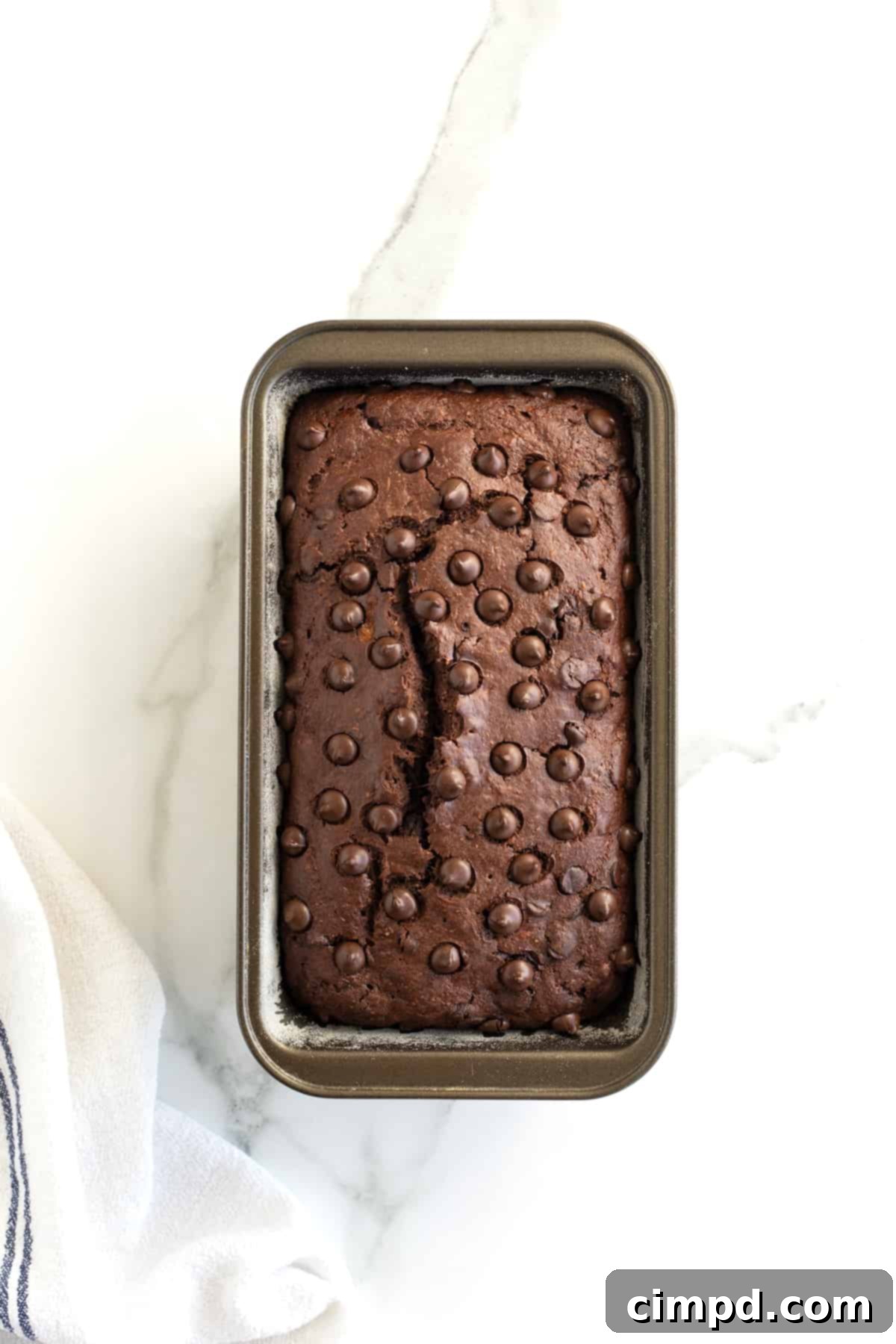 Guilt-Free Chocolate Banana Loaf 10 A baked loaf of healthy chocolate banana bread in a metal pan, showing a beautiful crack down the middle and melted chocolate chips on top.