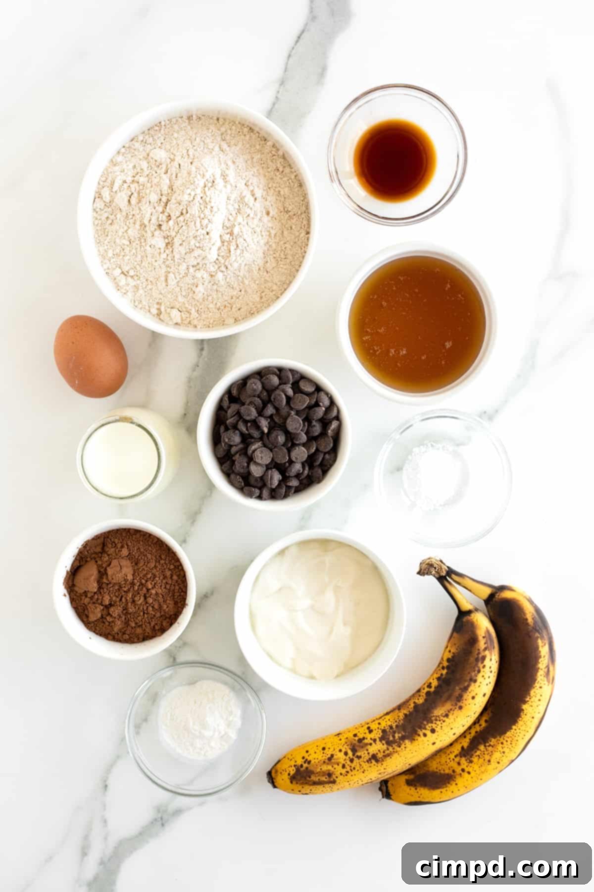 Guilt-Free Chocolate Banana Loaf 7 Ingredients for healthy chocolate banana bread, including whole wheat flour, honey, chocolate chips, and ripe bananas, arranged on a marble surface.