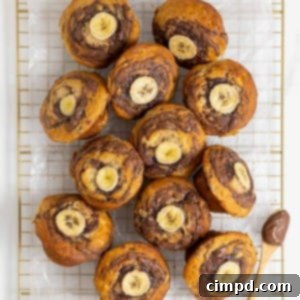 Nutella swirled banana muffins with a slice of banana on top resting on a parchment lined gold tone cooling rack.