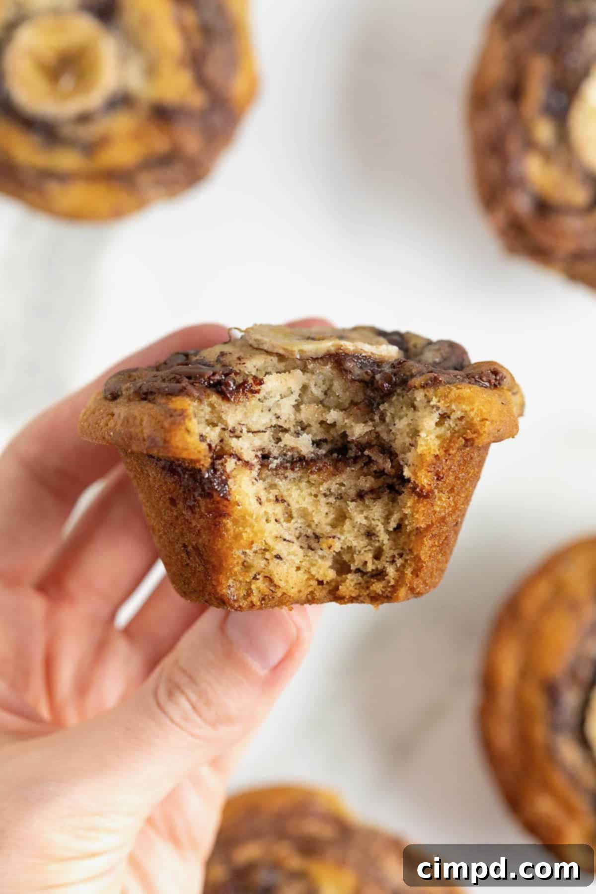 A hand holding a nutella swirled banana muffin with a bite out of it.