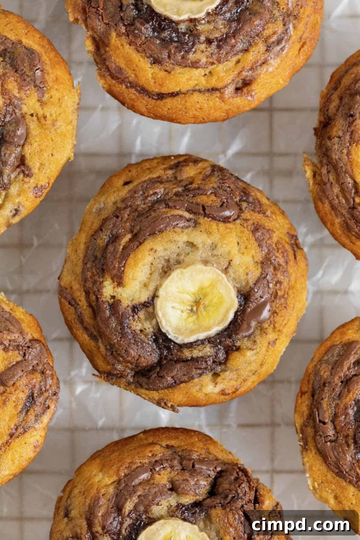 Nutella swirled banana muffins with a slice of banana on top resting on a parchment lined gold tone cooling rack.