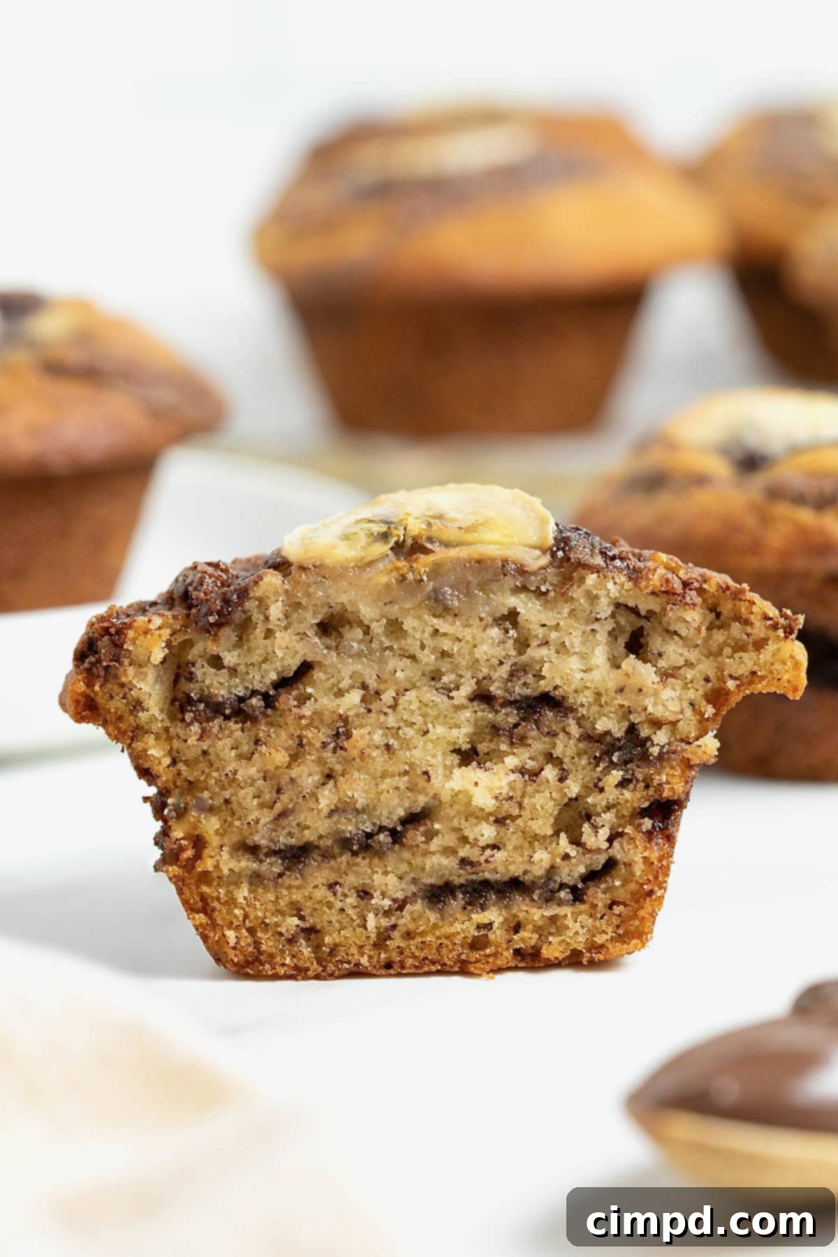 A nutella swirled banana muffin cut in half on a white marble counter.