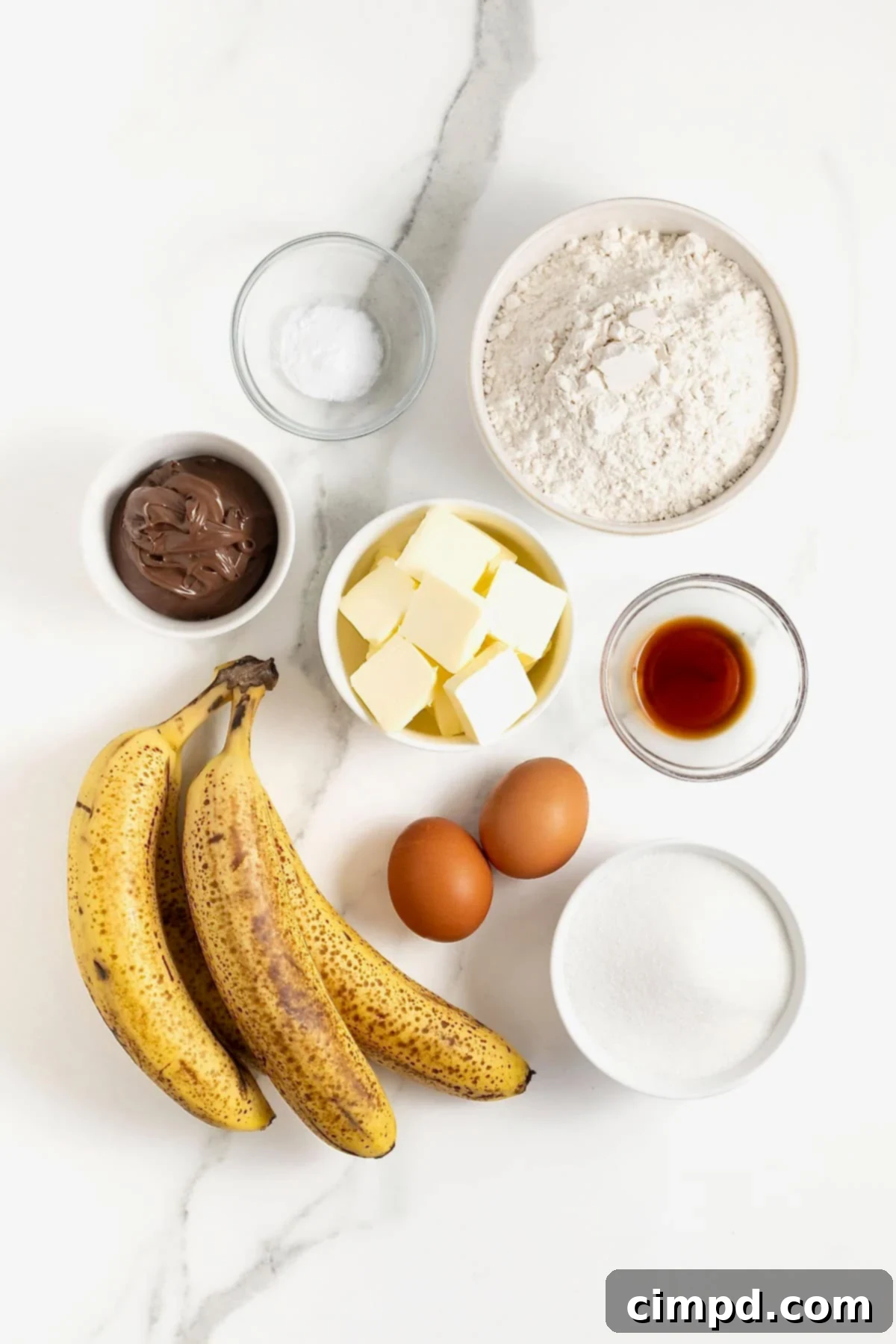 Ingredients to make Nutella swirled banana muffins in small glass dishes on a white marble counter.