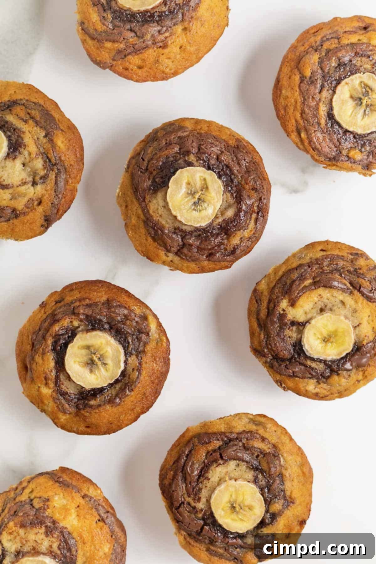Eight Nutella swirled banana muffins on a white marble counter.