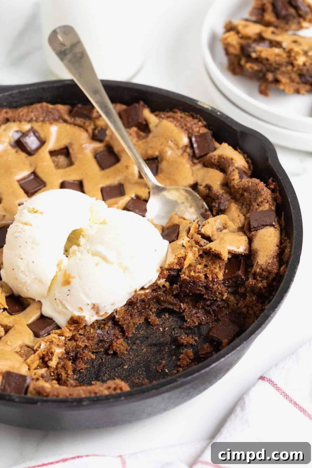 A chocolate chunk cookie in a large black skillet. There's a scoop of ice cream on top and a spoon stuck in it.