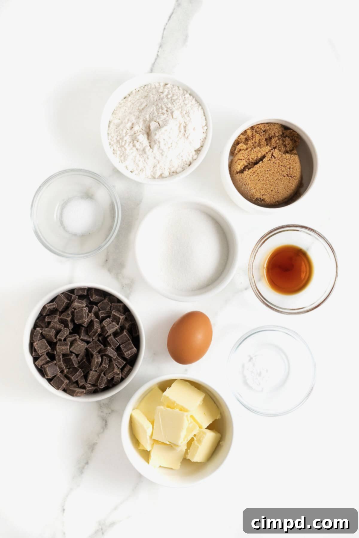 Ingredients to make a skillet chocolate chunk cookie in small glass dishes on a white marble counter.