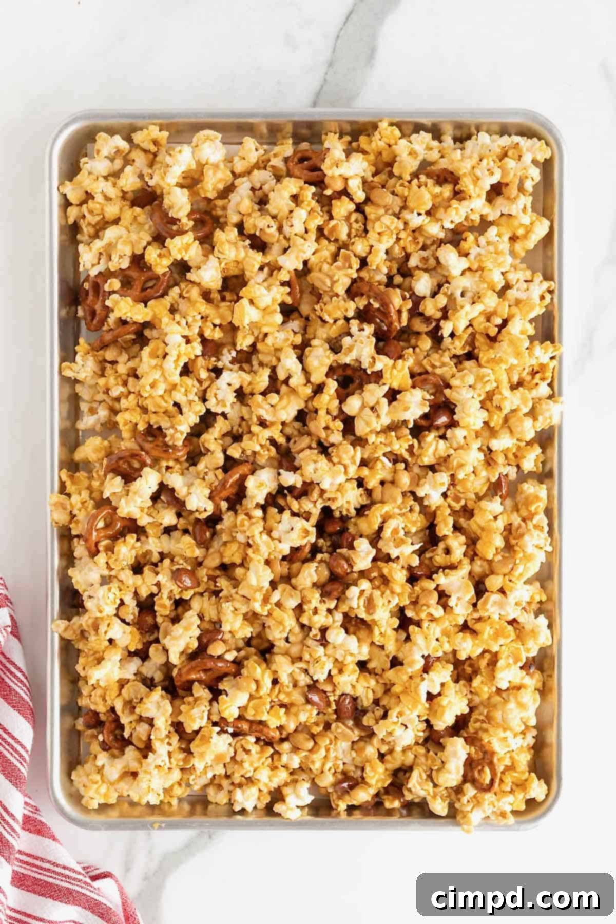 Caramel corn mix with peanuts and pretzels on a sheet pan.