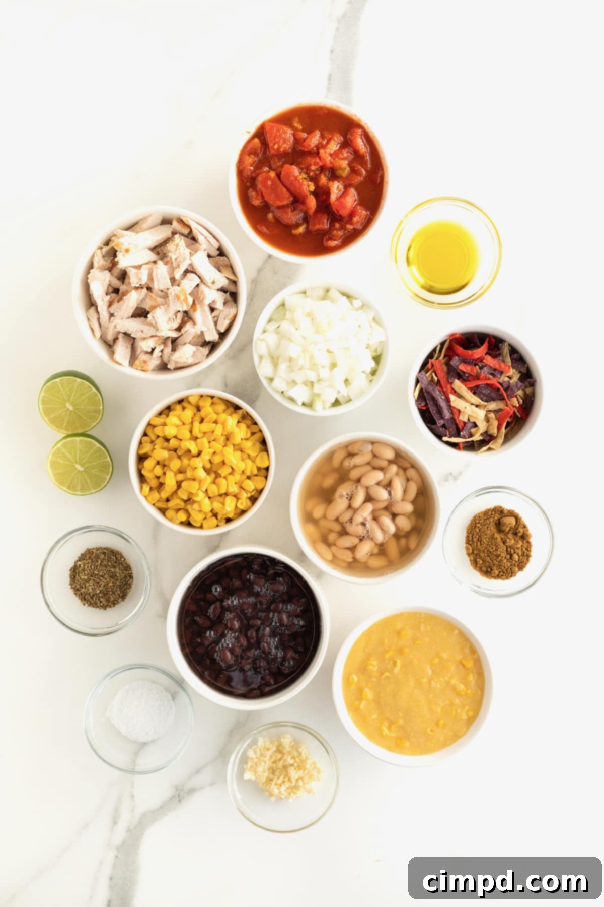 A perfectly arranged mise en place: small glass containers holding all the fresh ingredients needed for chicken tortilla soup, neatly displayed on a white kitchen counter.