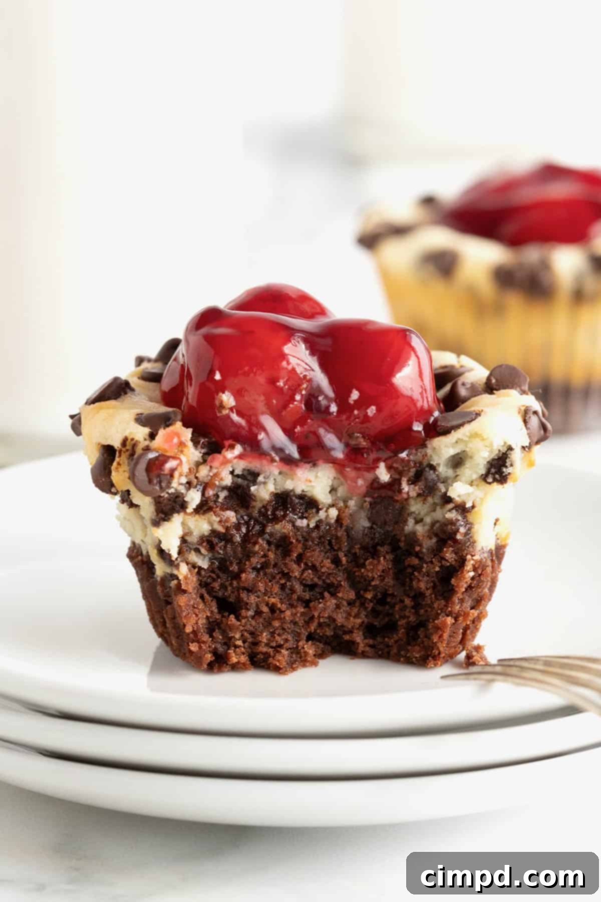 A Cherry Chocolate Chip Cheesecake Brownie Bite on white dessert plates, with a small bite taken out, revealing its delicious layers.