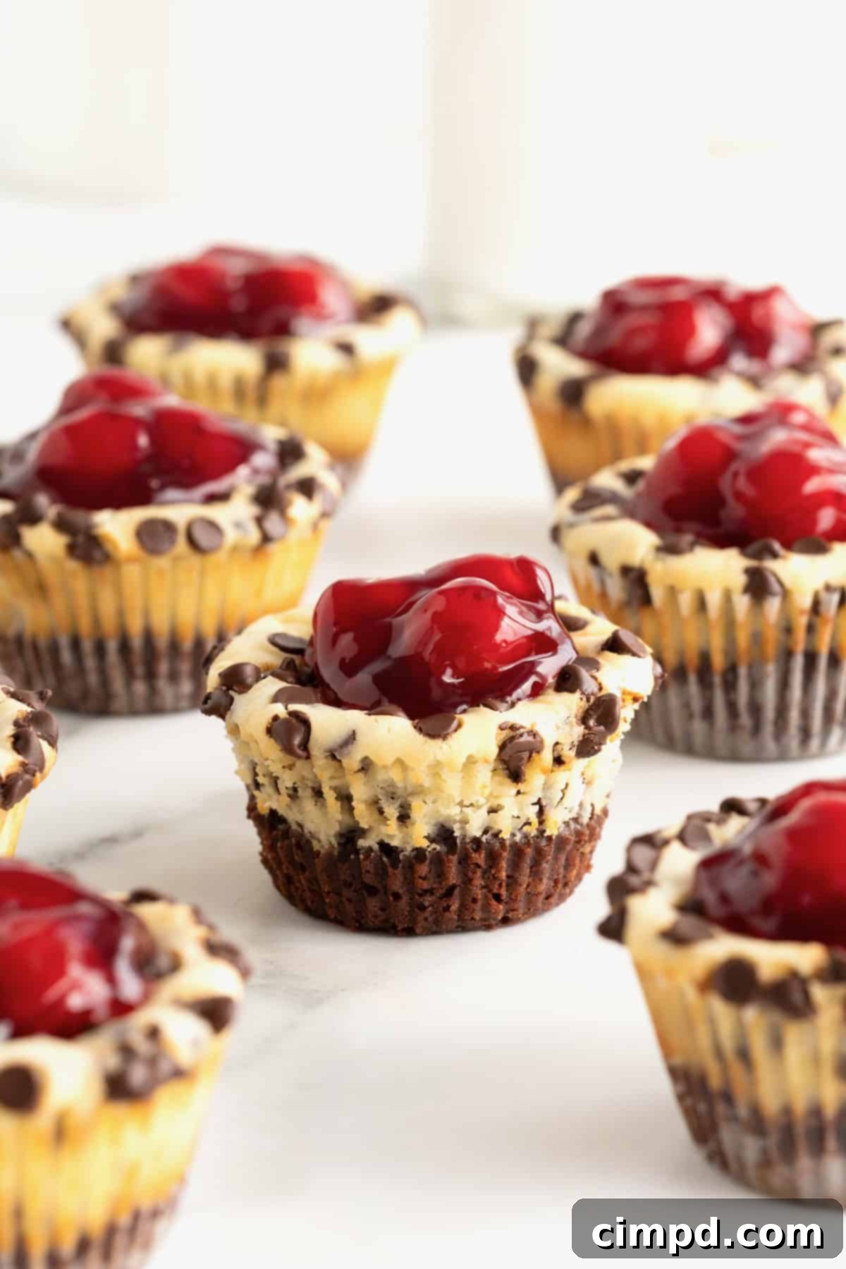 Nine delicious Cherry Chocolate Chip Cheesecake Brownie Bites, each topped with a glistening cherry, neatly arranged on a piece of parchment paper.