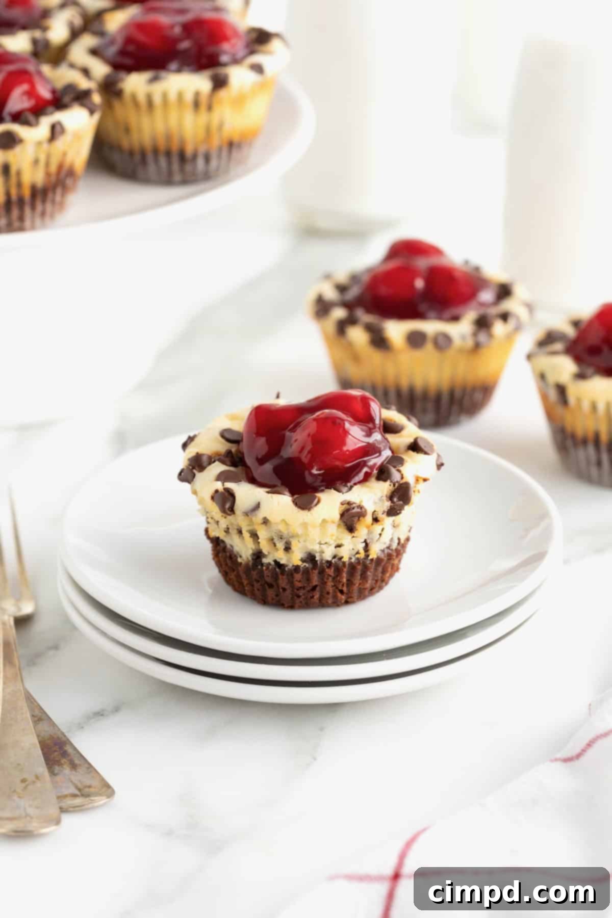 A single Cherry Chocolate Chip Cheesecake Brownie Bite, beautifully presented on a white dessert plate, with the top adorned with luscious cherries.
