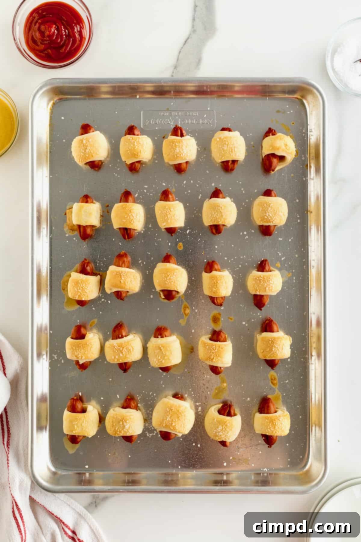 Sausage Swaddles 8 An aluminum baking sheet holds 25 perfectly baked pigs in a blanket, arranged in neat rows, golden and ready to be served.