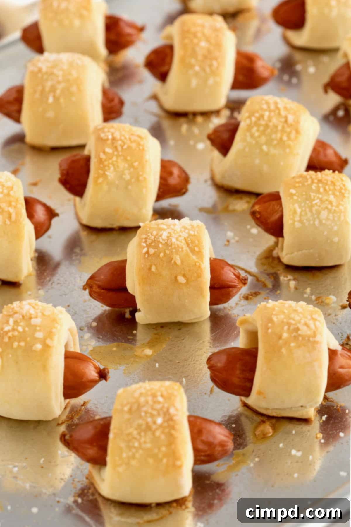 Sausage Swaddles 9 Freshly baked pigs in a blanket resting on an aluminum baking sheet, golden brown and ready to be served or stored.