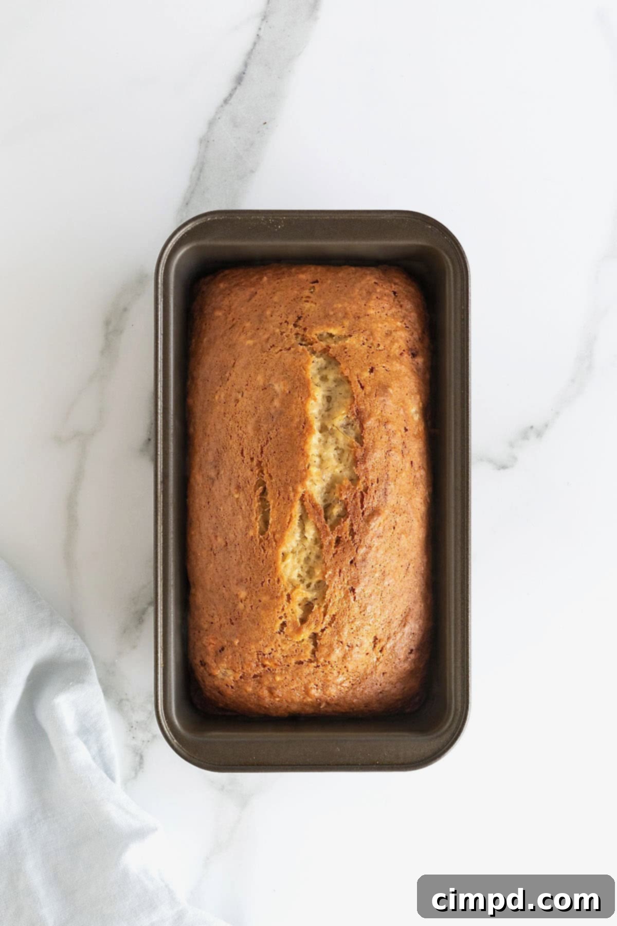 Next Level Brown Butter Banana Bread 10 A loaf of brown butter banana bread in a dark aluminum loaf pan on a white marble counter.