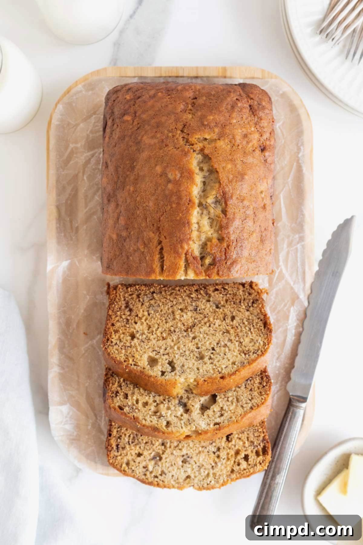 Next Level Brown Butter Banana Bread 11 A sliced loaf brown butter banana bread loaf on a parchment covered wooden cutting board.