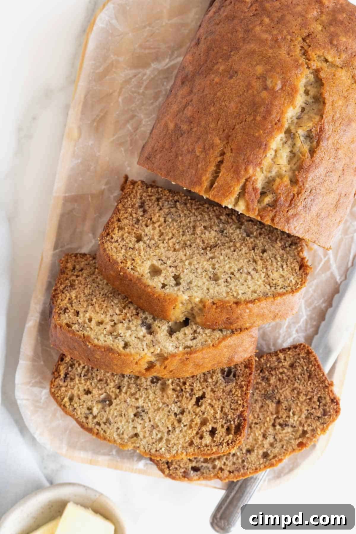 Next Level Brown Butter Banana Bread 12 A sliced loaf brown butter banana bread loaf on a parchment covered wooden cutting board.