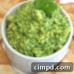 A small bowl of creamy blender guacamole next to fresh cilantro and lime wedges.