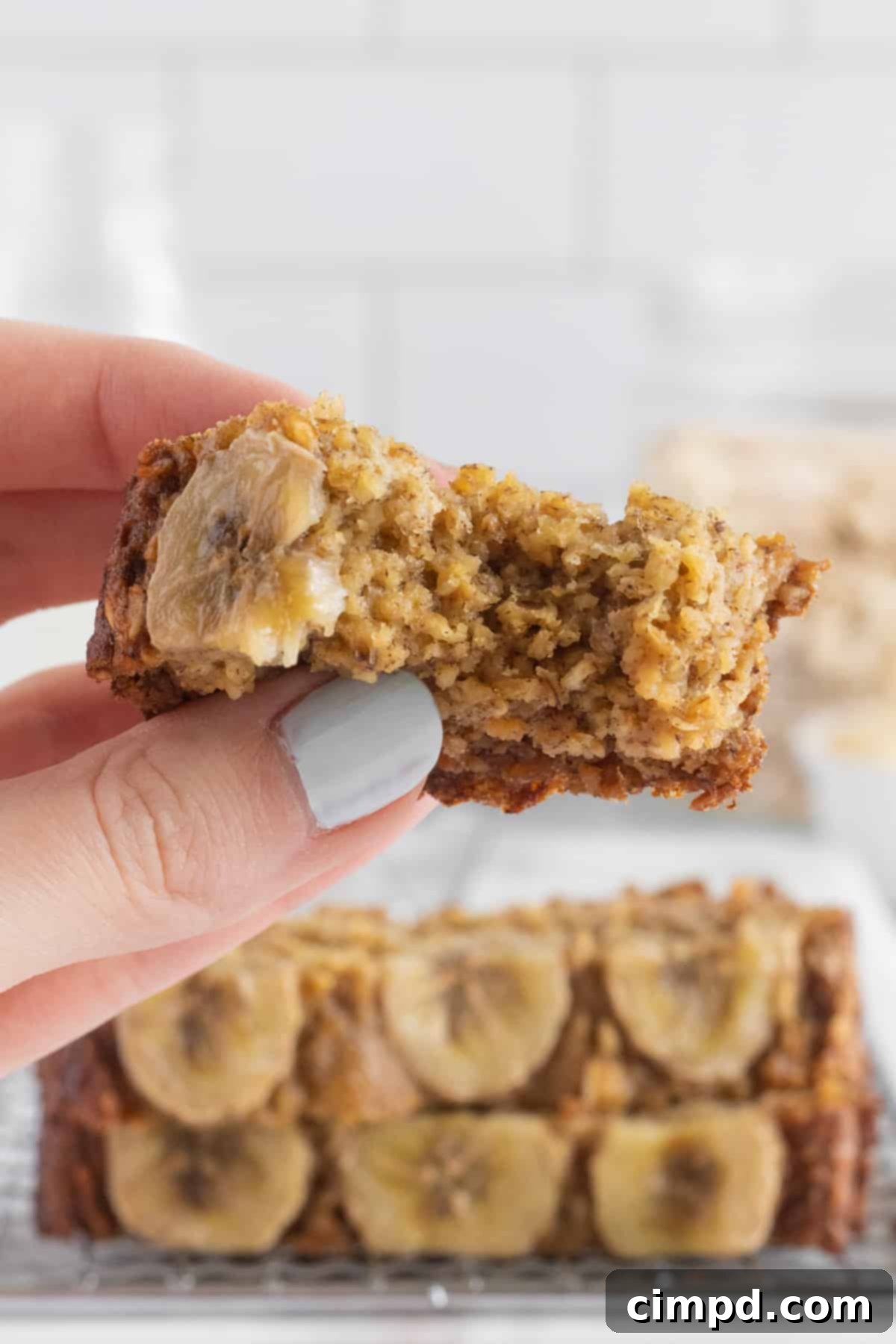 A hand holding a slice of flourless banana bread with a bite out of it, showing its moist texture.