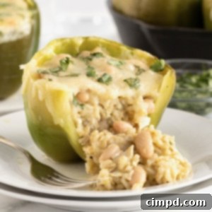 A stuffed green pepper with rice, white beans and white cheese melted on top. The pepper is on a small white plate with fork next to it on the left.