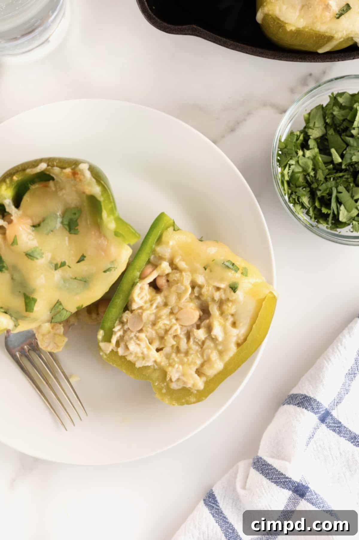 A green bell pepper, expertly cut in half to reveal its rich and hearty interior. The cross-section clearly displays the flavorful stuffing, a blend of fluffy rice, tender shredded chicken, and creamy white beans, illustrating the satisfying texture and density of the filling.