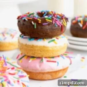 Effortless Cake Mix Baked Donuts 16 Three donuts in a stack. The top donut is chocolate with chocolate frosting. The middl donut is vanilla with white icing and the bottom donut is vanilla with pink icing. All the donuts have rainbow sprinkles.