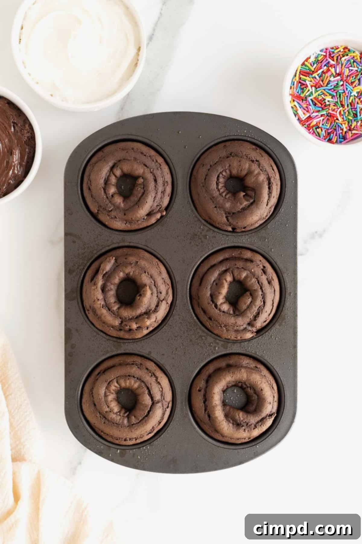 Effortless Cake Mix Baked Donuts 8 Golden-brown chocolate cake donuts perfectly baked in a non-stick donut pan, ready to be removed and glazed.
