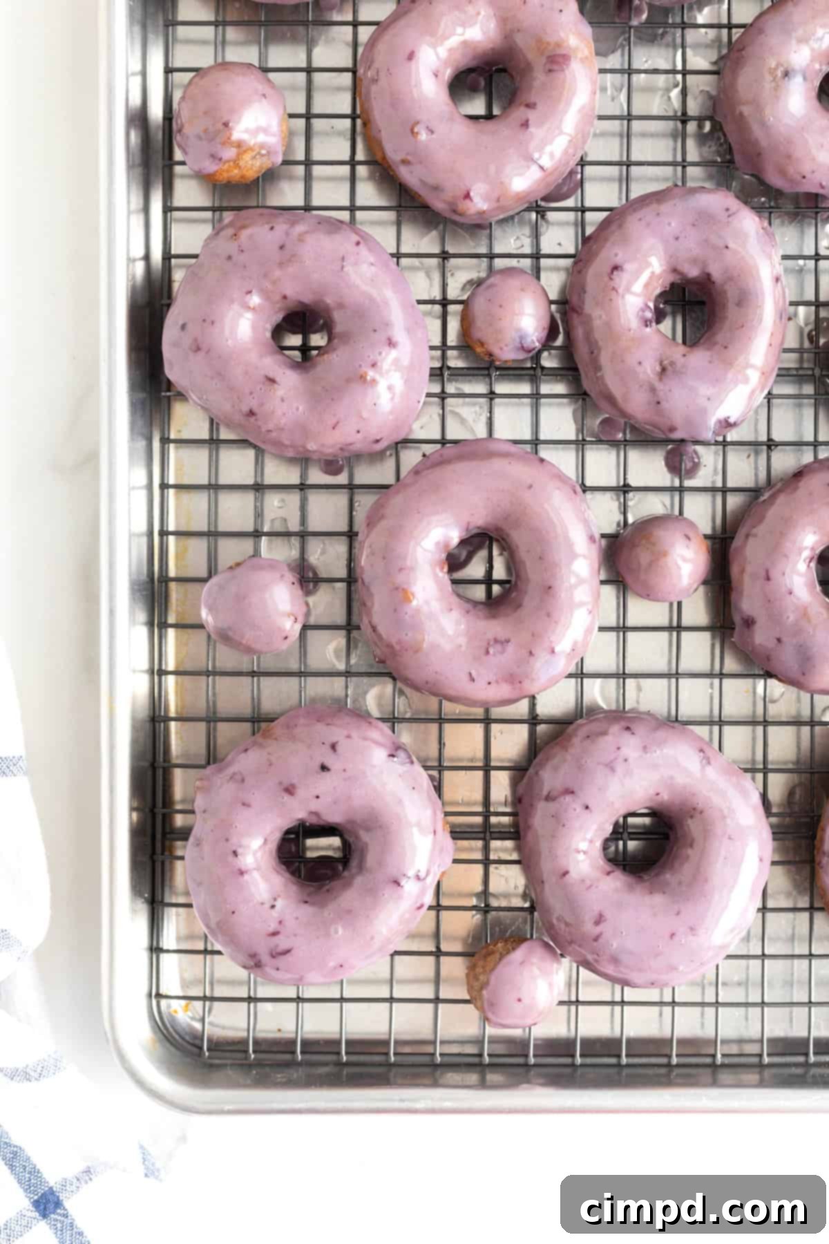 A batch of blueberry donuts with a smooth blueberry glaze resting on a wire rack inside a rimmed baking sheet, ready for serving or cooling.