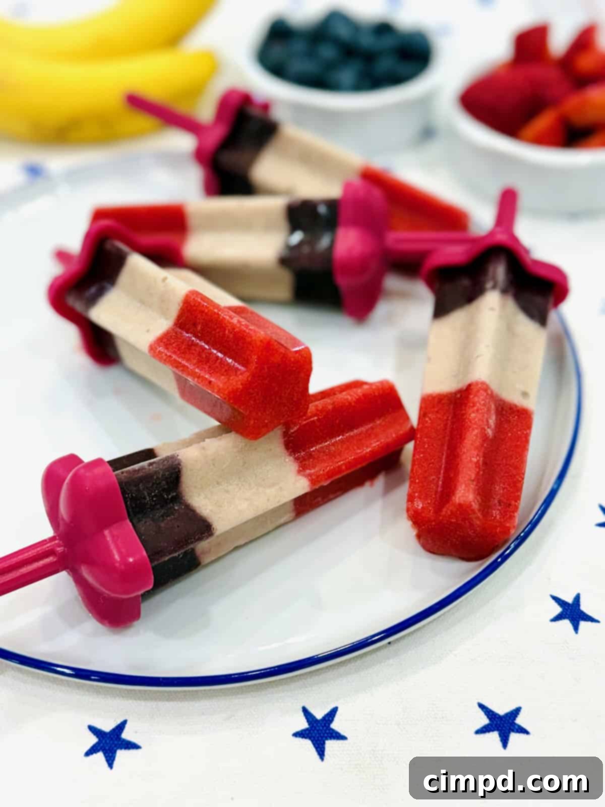 Five star-shaped fruit pops on a white serving plate, showcasing red, white, and blue layers.