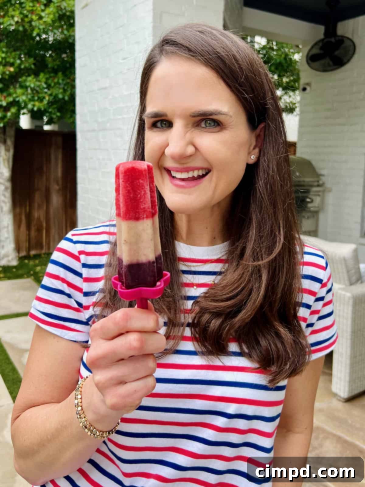 Maegan Brown, wearing a red, white, and blue striped shirt, holds a tri-color patriotic fruit pop with a joyous expression.
