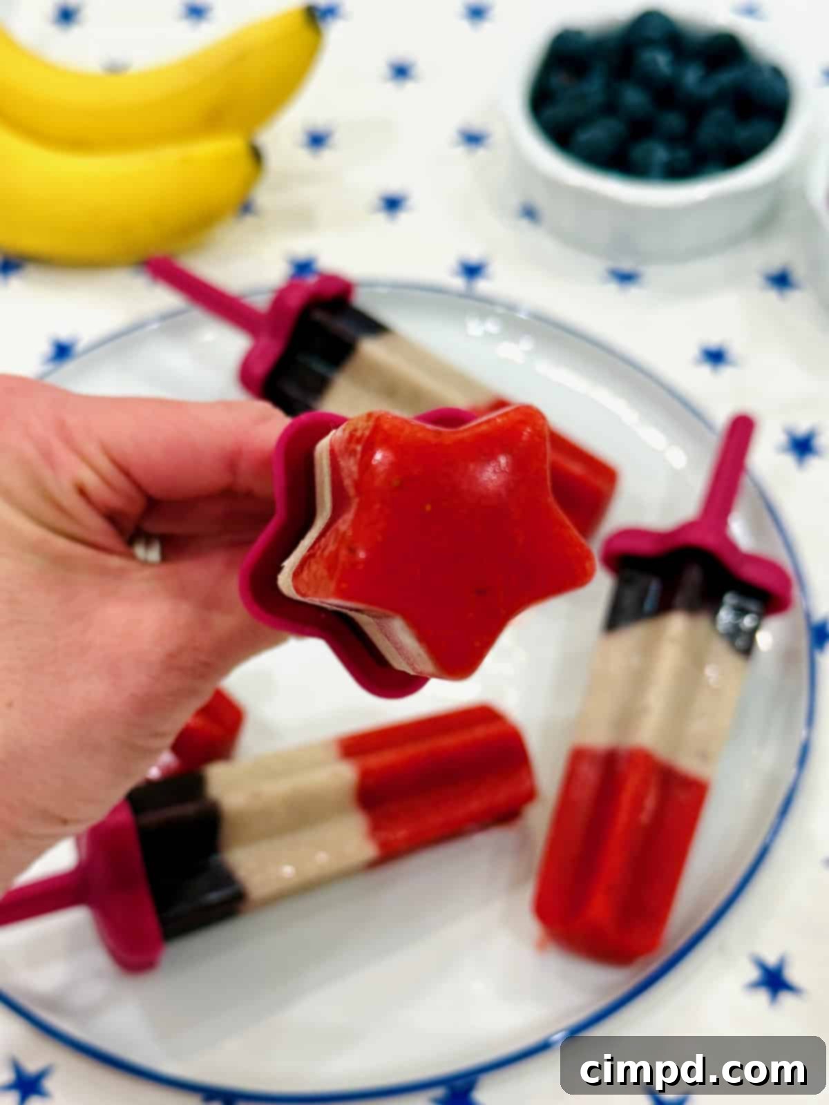A hand holds a single star-shaped frozen fruit pop against a soft background.