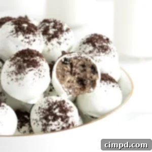 A large white serving bowl filled with cake balls coated in white coating and dusted with cookie crumbs. One of the cake balls has a bite out of it revealing the Oreo cookie cake inside.