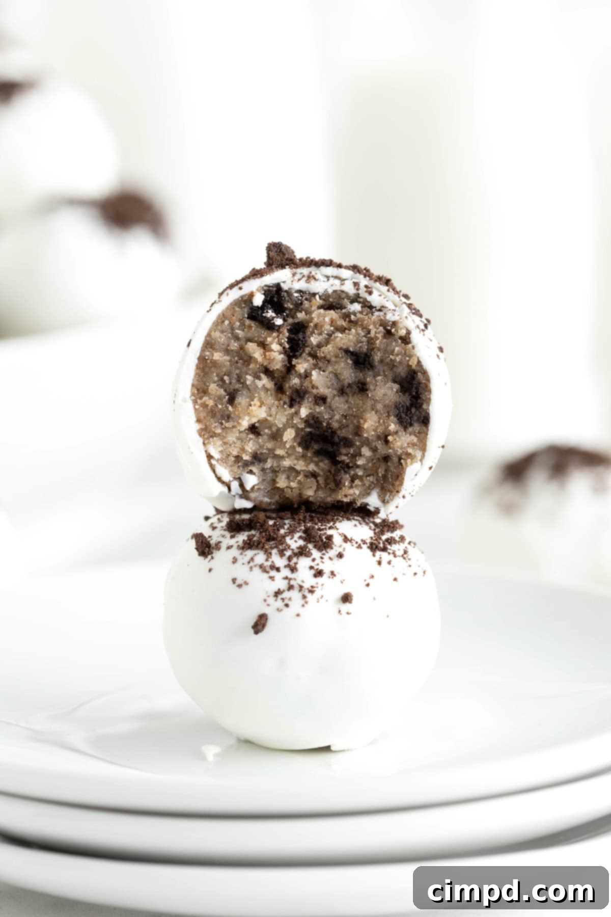 Two cake balls stacked on a small white rimmed plate. The top ball has a bite out of it.